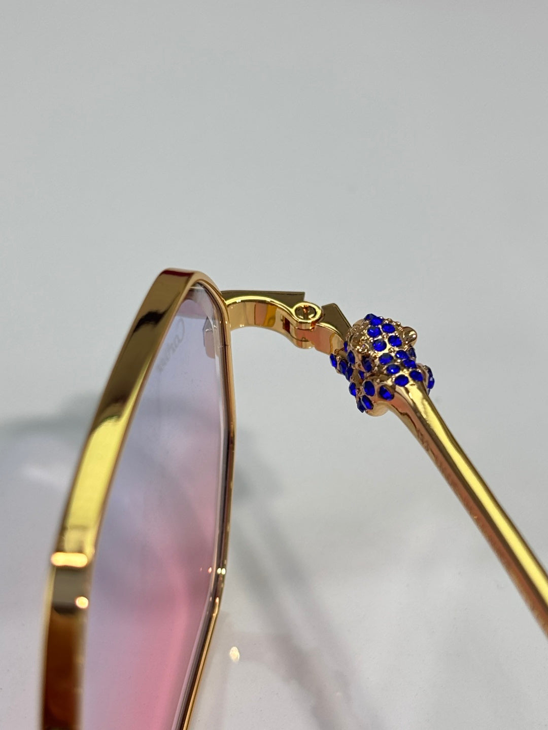 Cartier eyeglasses side arm with gold finish and blue jeweled emblem detail.