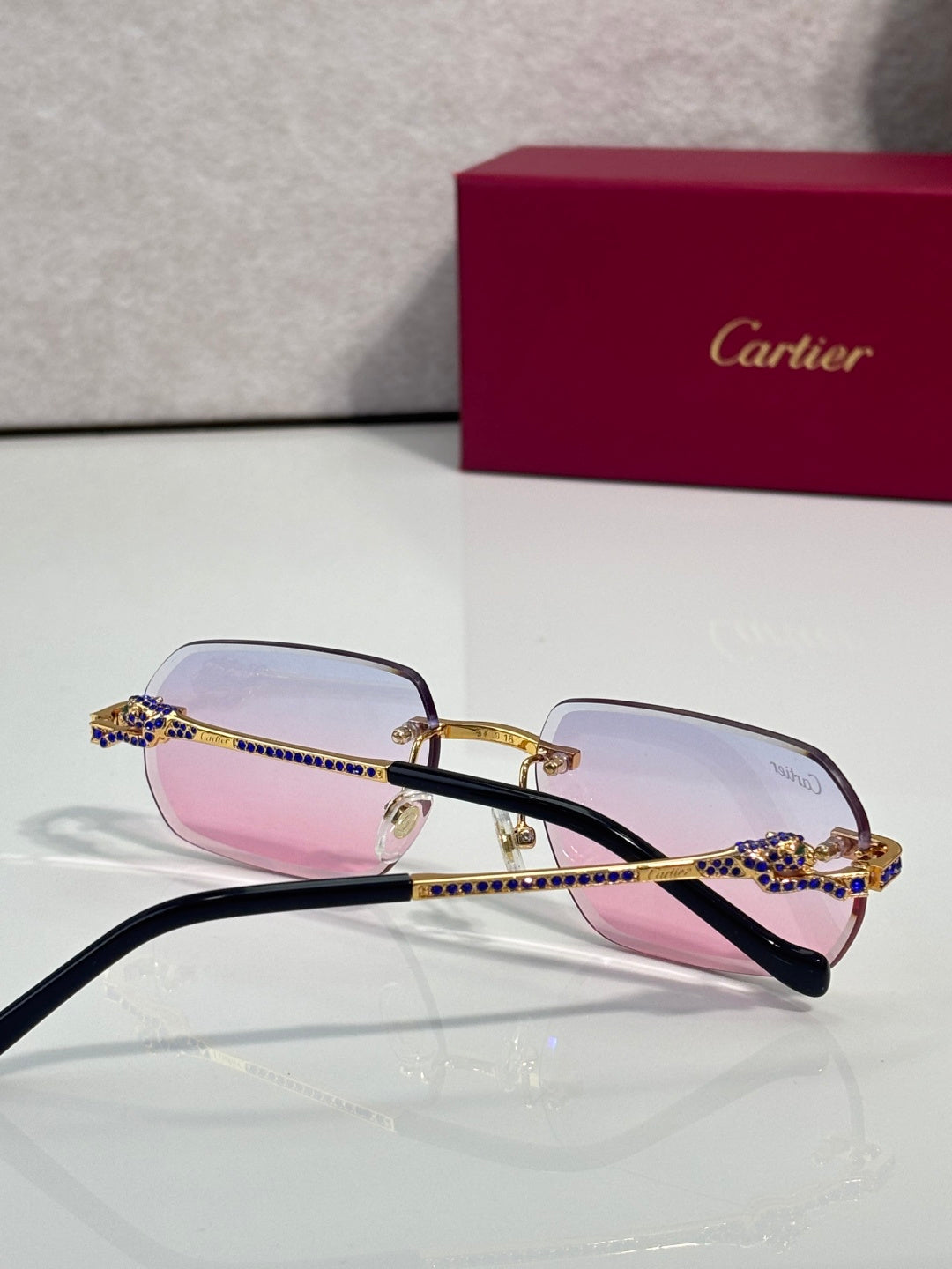 Cartier eyeglasses with black temples and pink lenses, blue gem crown detail
