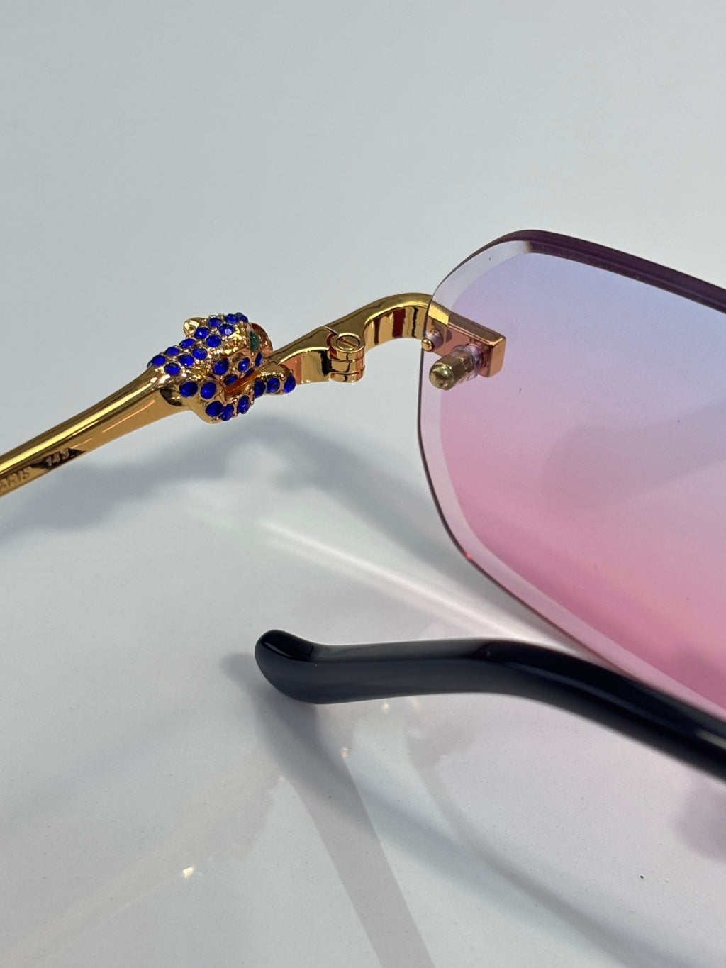 Gold eyeglass temple with blue jeweled detail and pink lens close-up