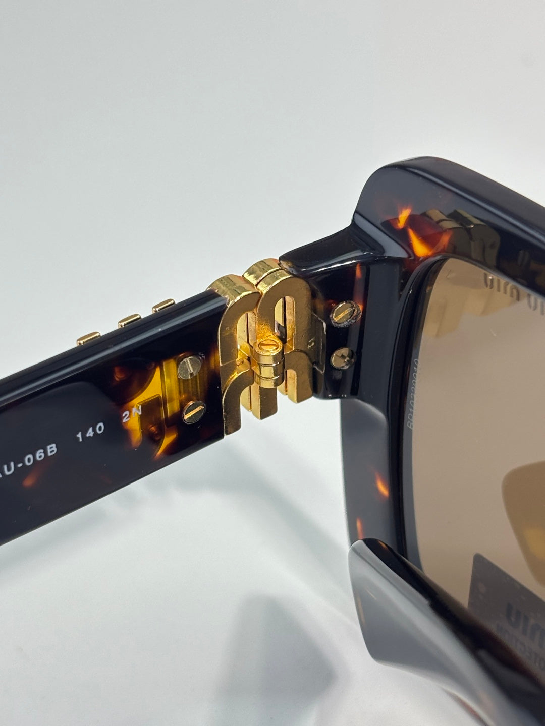 MiuMiu sunglasses hinge close-up with gold hardware and tortoiseshell arm