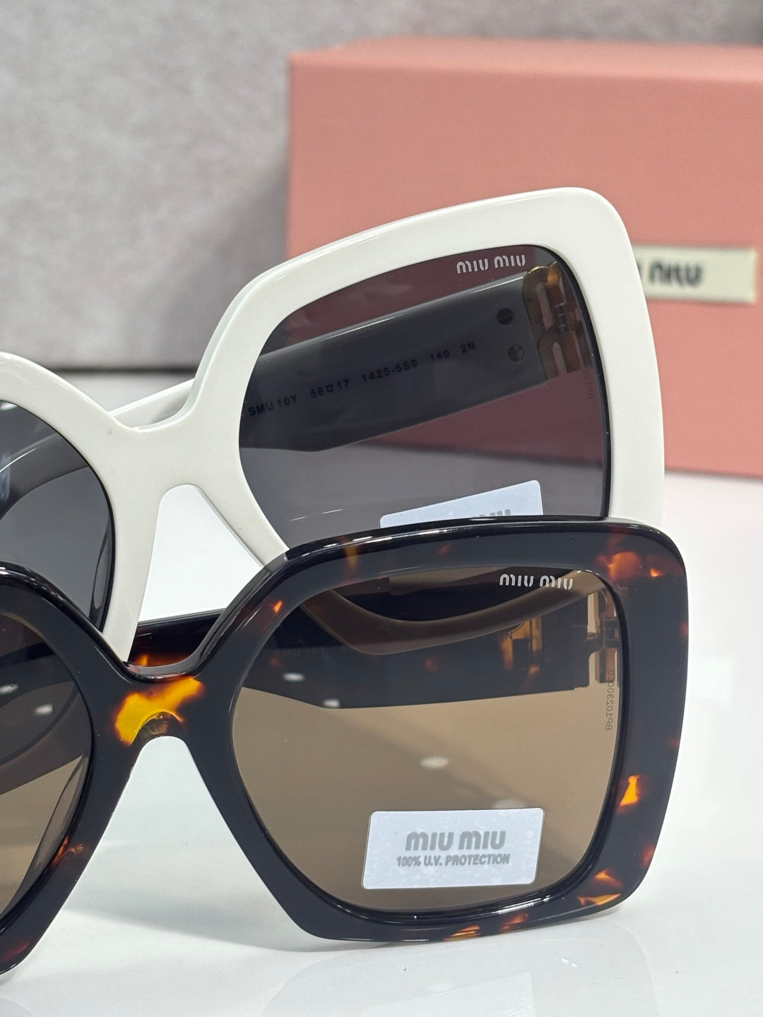 MiuMiu square sunglasses, white frame with dark lens; tortoiseshell pair behind