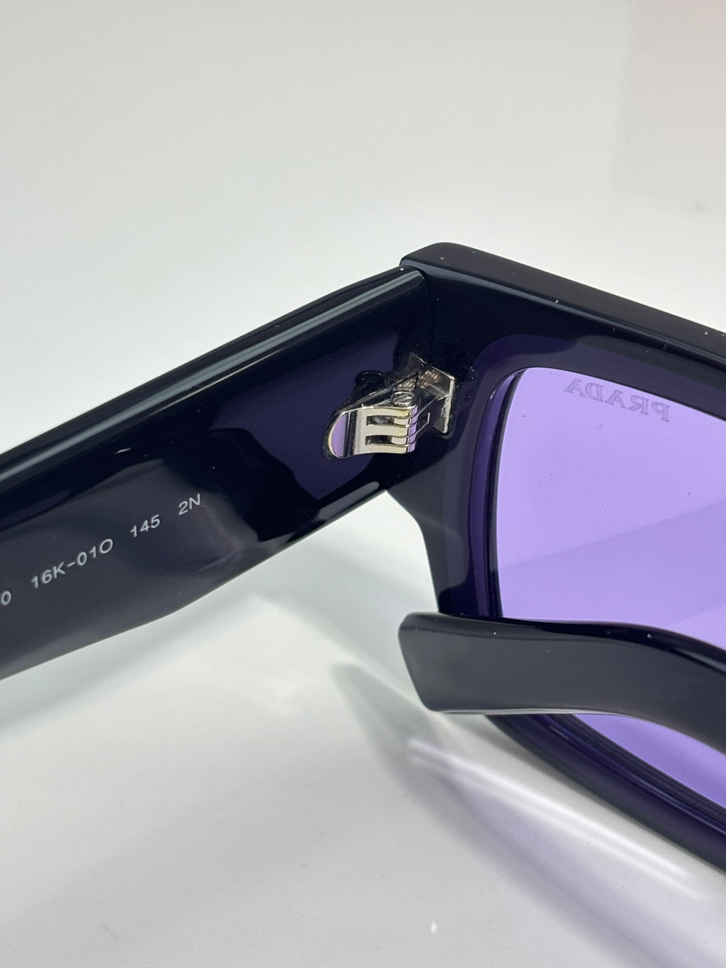 Black sunglasses with purple lenses, hinge detail on side temple
