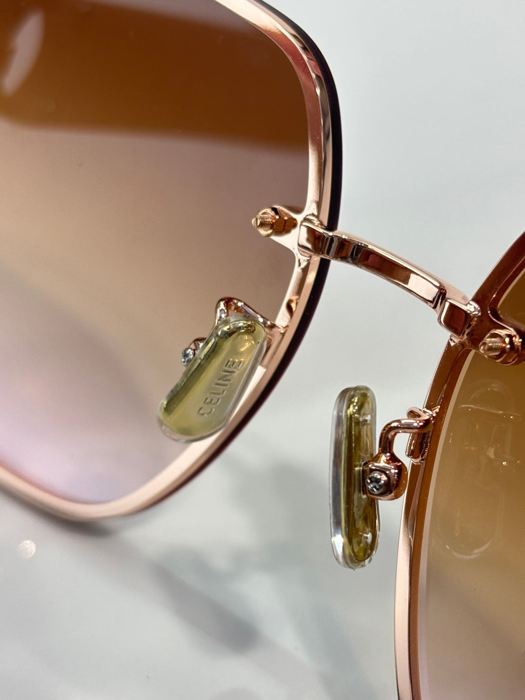 Celine sunglasses close-up: gold hinge hardware with tinted lenses and temple.
