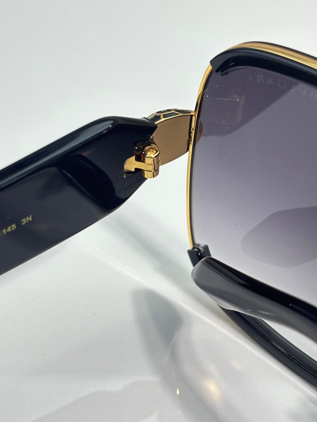 Sunglasses side close-up: gold bridge and black temple with logo detail