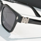 Black square sunglasses close-up: rhinestone emblem and silver hinge