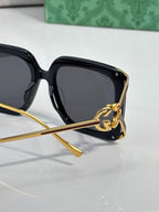 Black square sunglasses with gold-tone accents and circular logo charm at side.