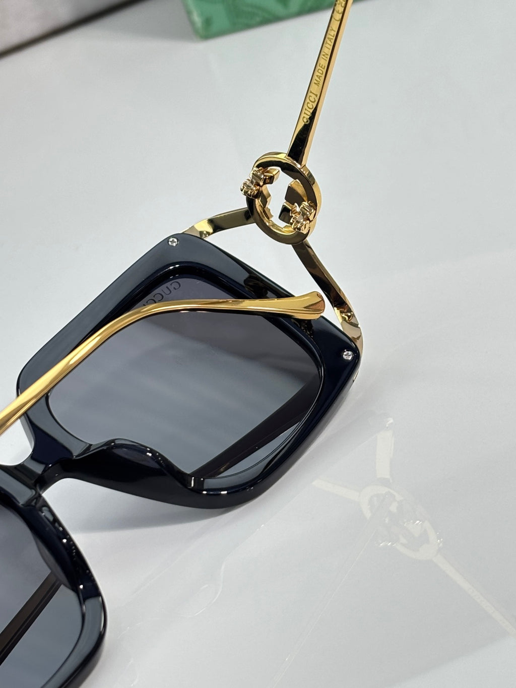 Black sunglasses close-up on gold-tone hinge hardware and dark lens.