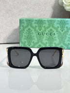 Square black sunglasses with dark lenses and gold-tone side detailing.