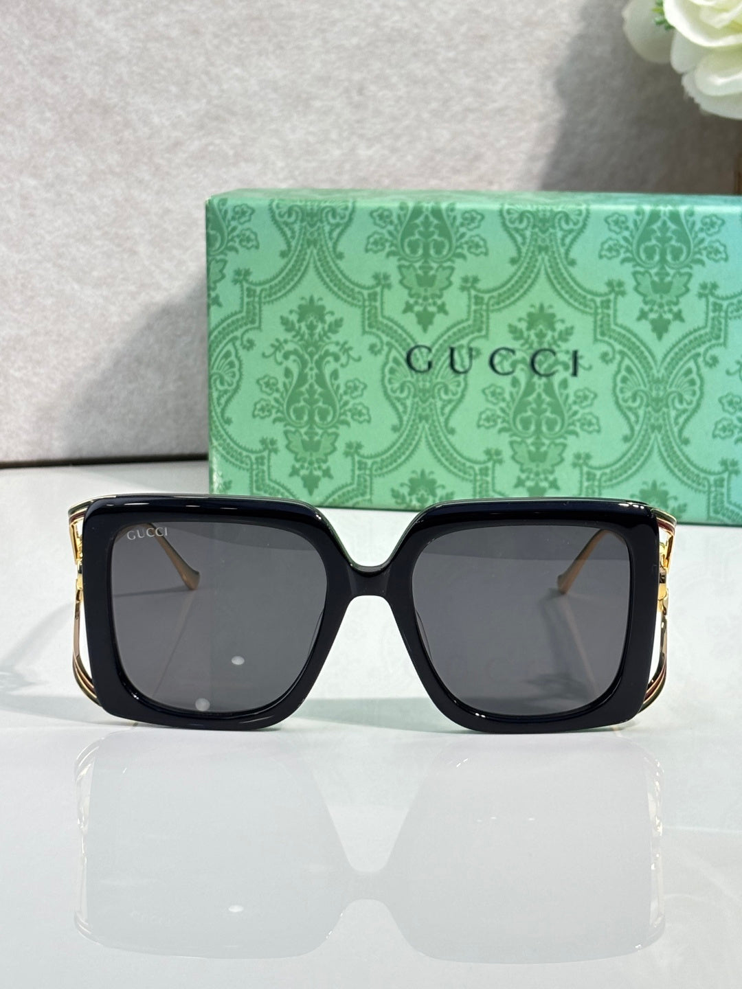 Square black sunglasses with dark lenses and gold-tone side detailing.