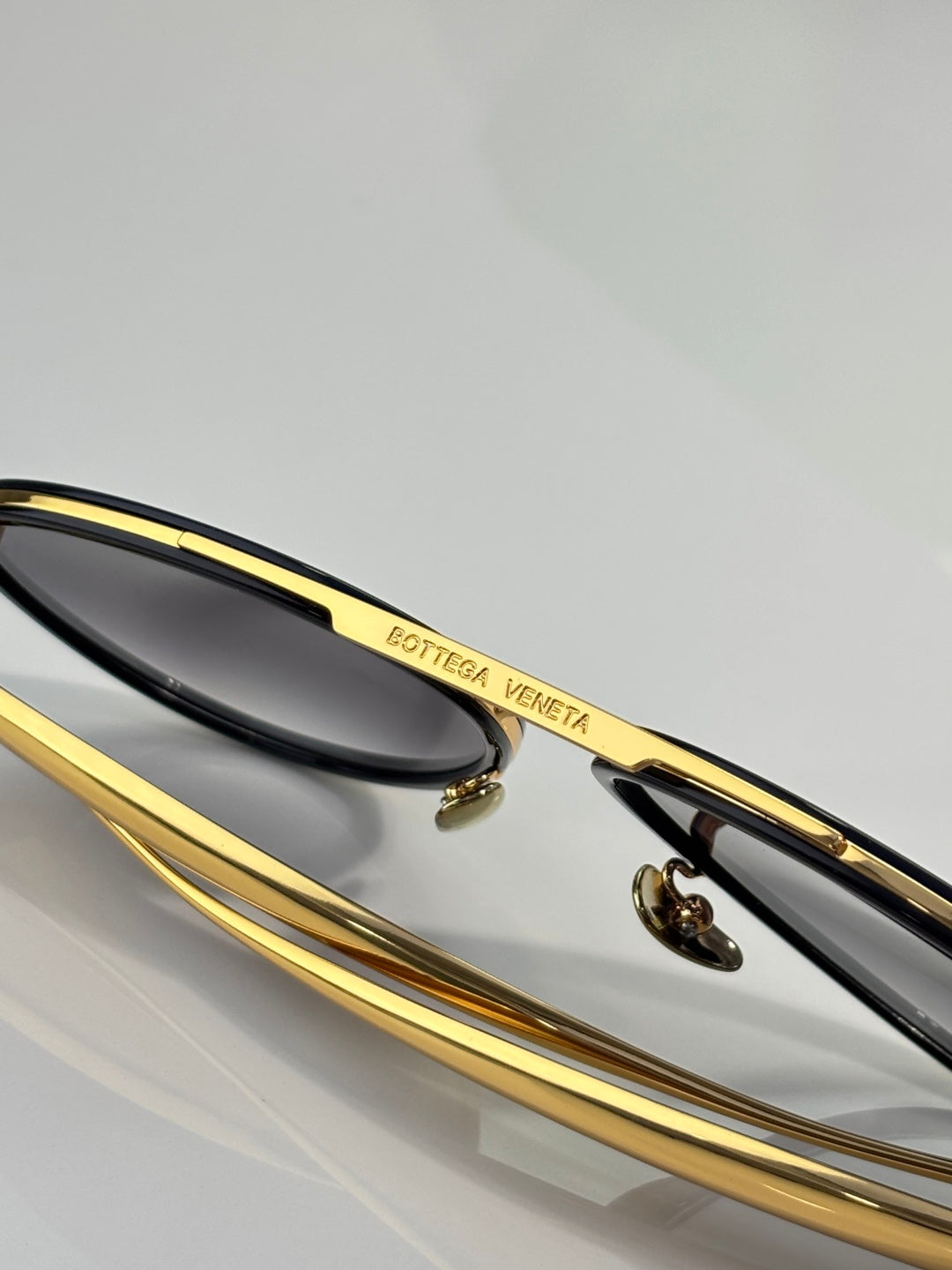 Bottega Veneta sunglasses close-up with gold bar detail and dark lens