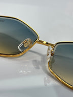 Gold-rim sunglasses close-up, dark tinted lens with engraved hinge logo