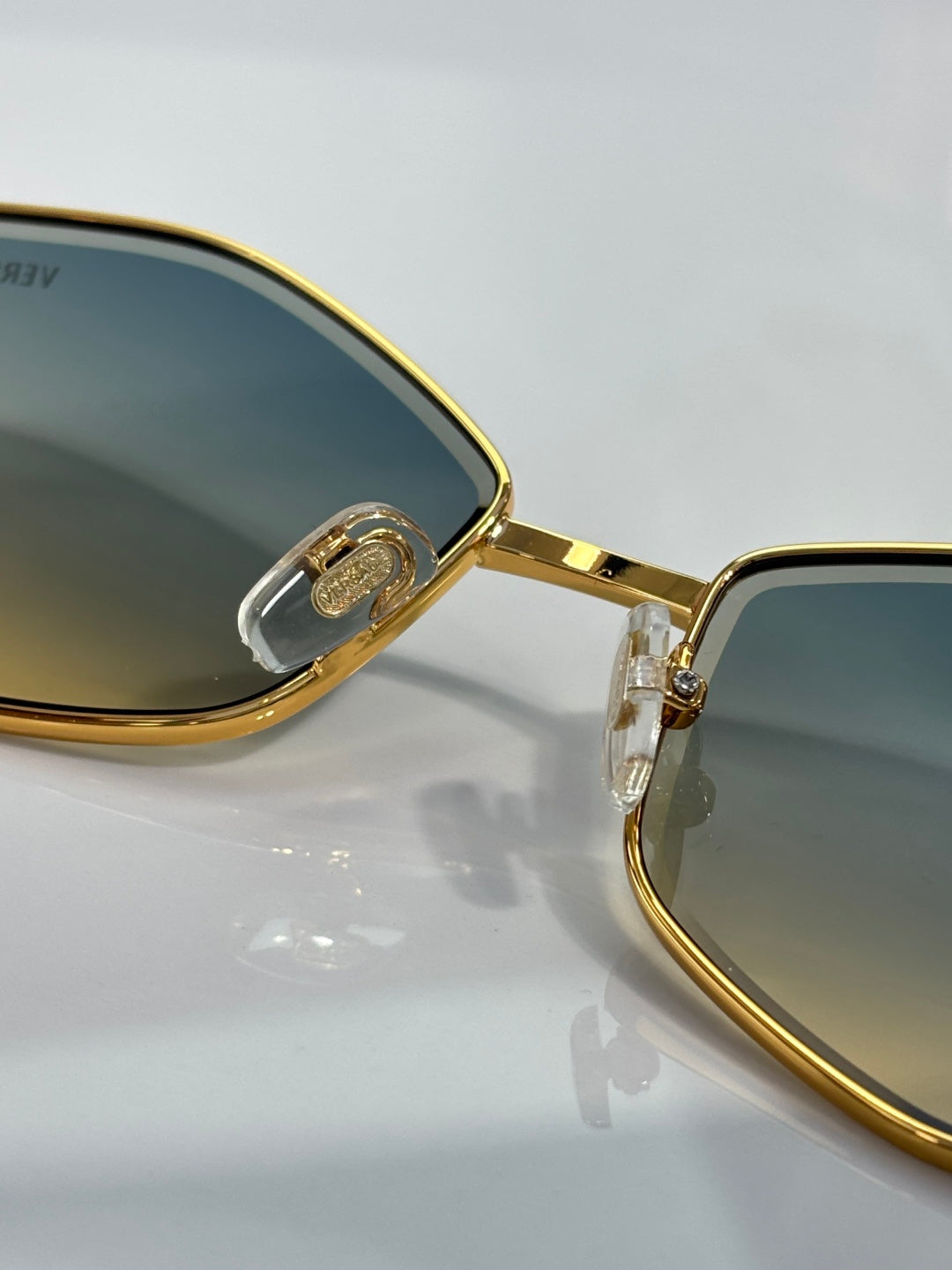 Gold-rim sunglasses close-up, dark tinted lens with engraved hinge logo