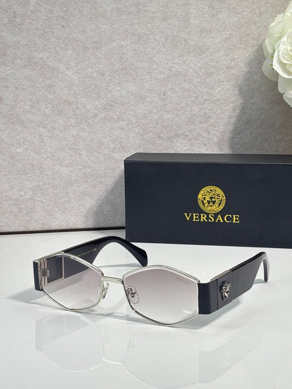 Sunglasses with light silver frame, dark lenses, gold logo detail on temple