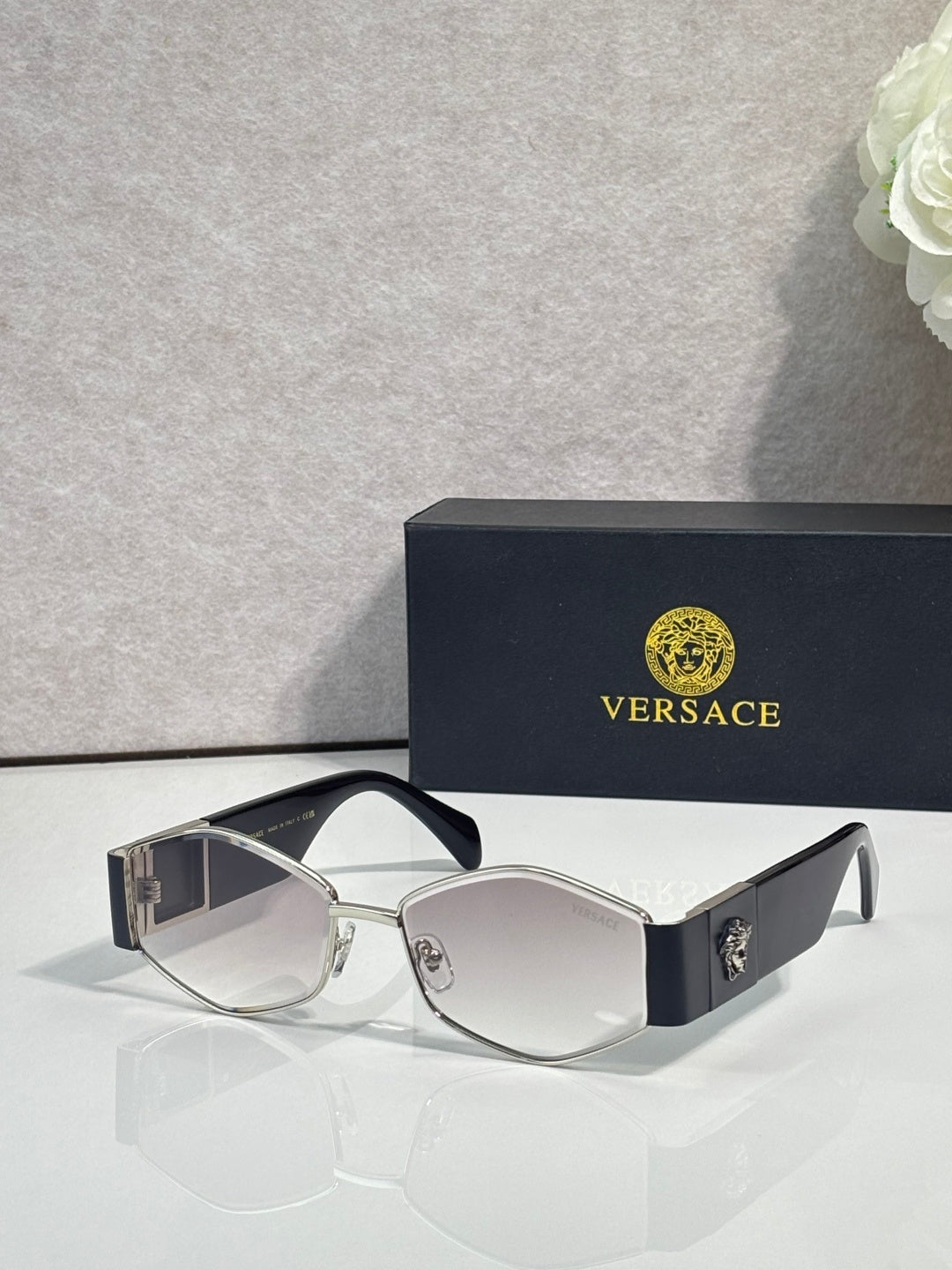 Sunglasses with light silver frame, dark lenses, gold logo detail on temple