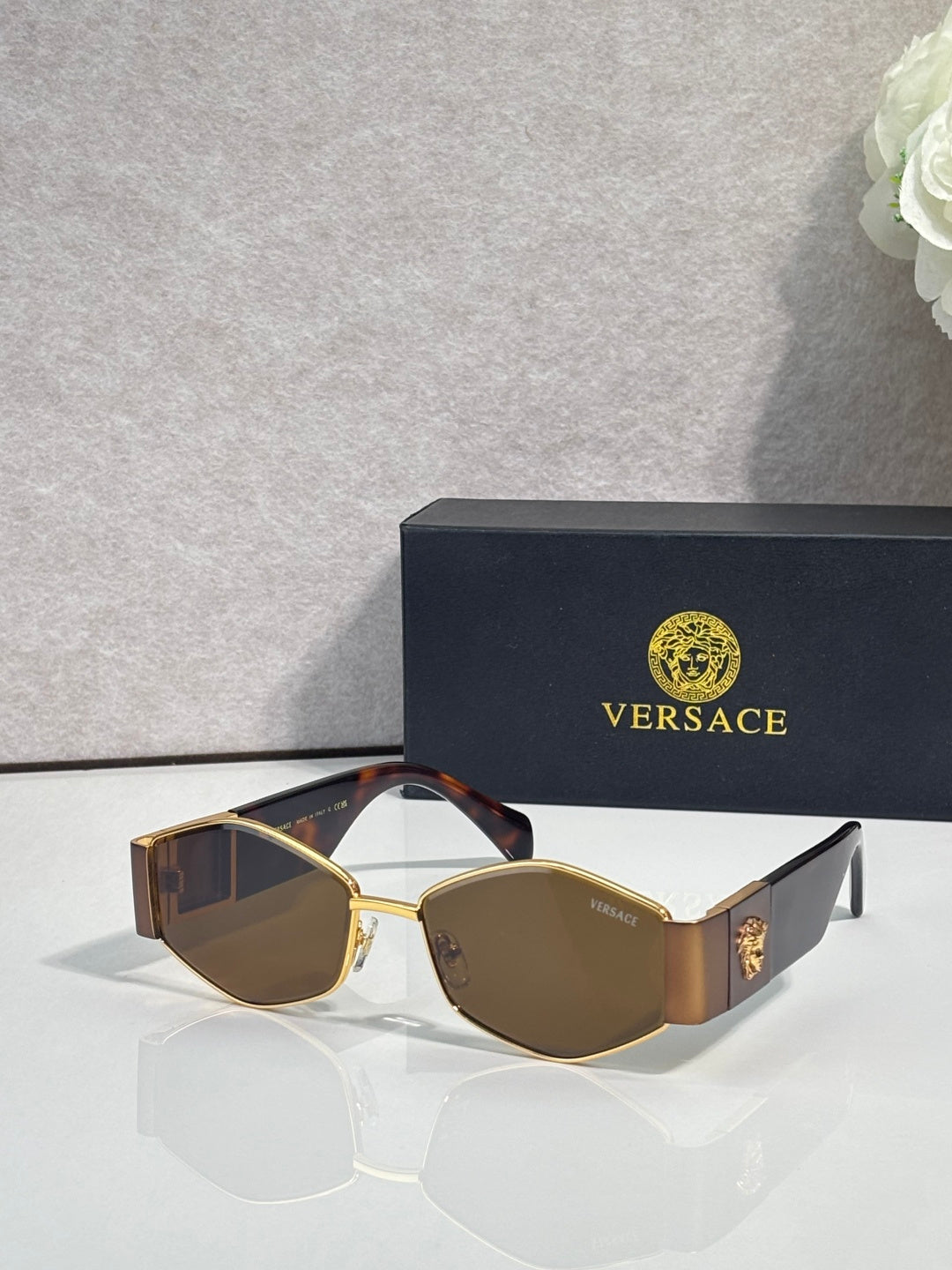 Sunglasses with gold frame, dark brown lenses, patterned temple, gold logo detail