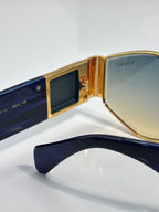 Sunglasses close-up with gold frame and blue temple, dark tinted lens