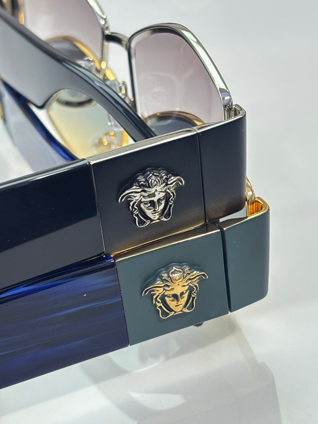 Sunglasses close-up with navy frame and gold hinge, Medusa logo detail