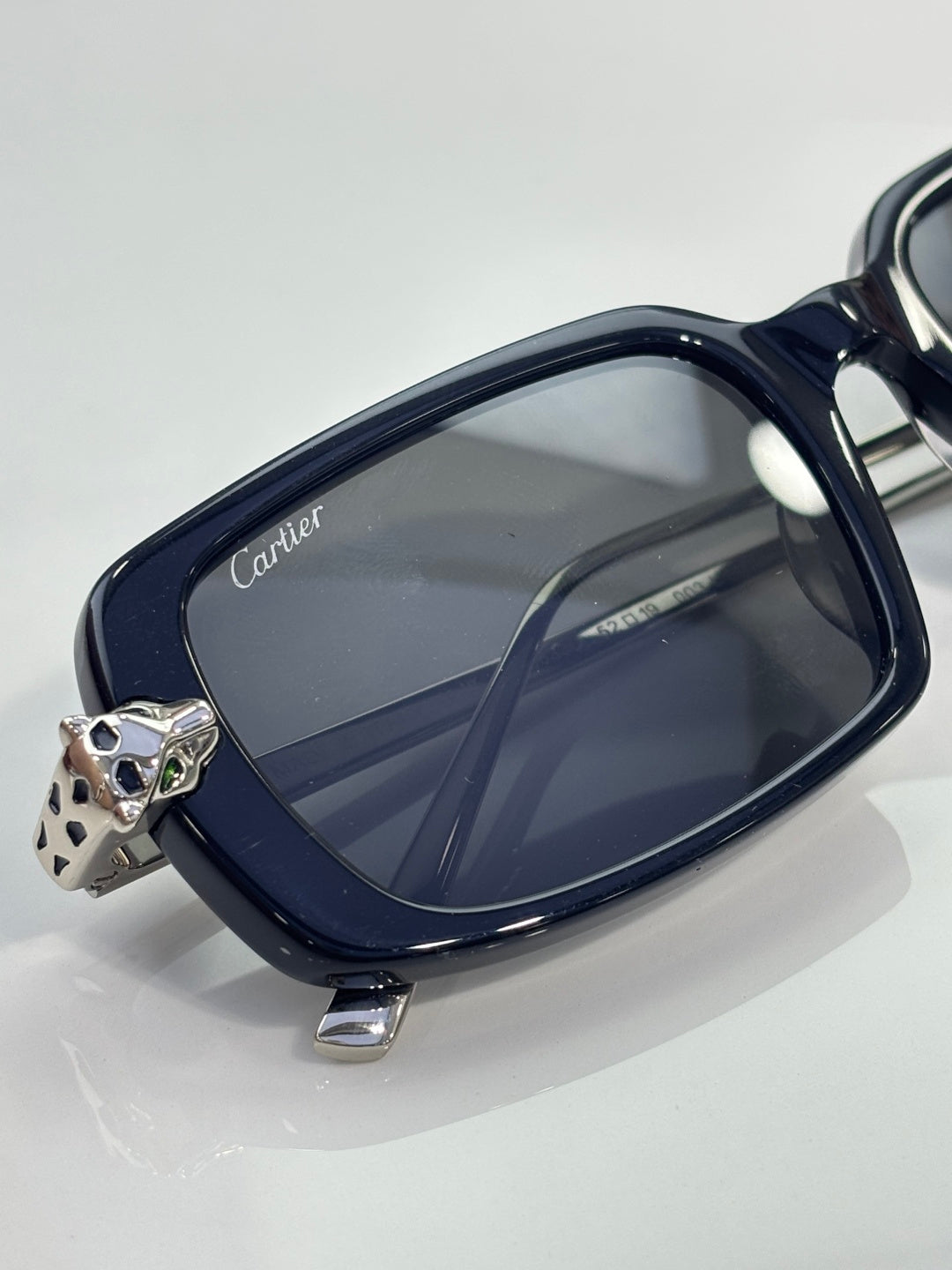 Navy eyeglasses close-up with oval frame, Cartier logo temple and metal charm