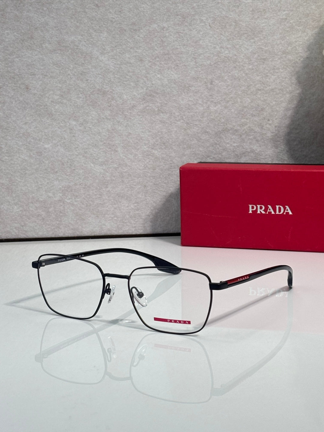 Black eyeglasses with clear lenses, red logo bar, and metal hinge details