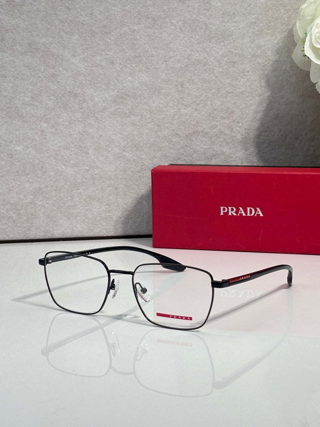 Black eyeglasses with clear lenses and red logo bar on the temple