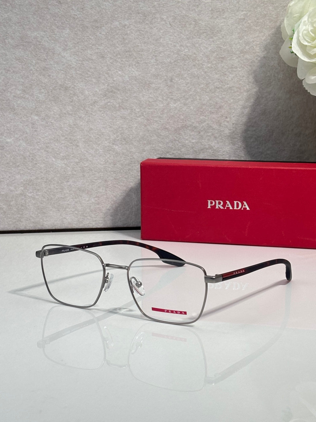 Black eyeglasses with clear lenses and red logo accent on the temple
