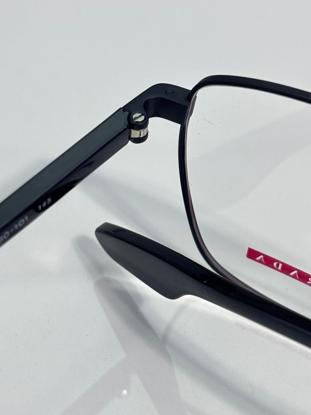 Black eyeglasses showing hinge hardware and small red logo accent on temple