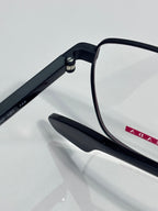 Black eyeglasses showing hinge hardware and small red logo accent on temple
