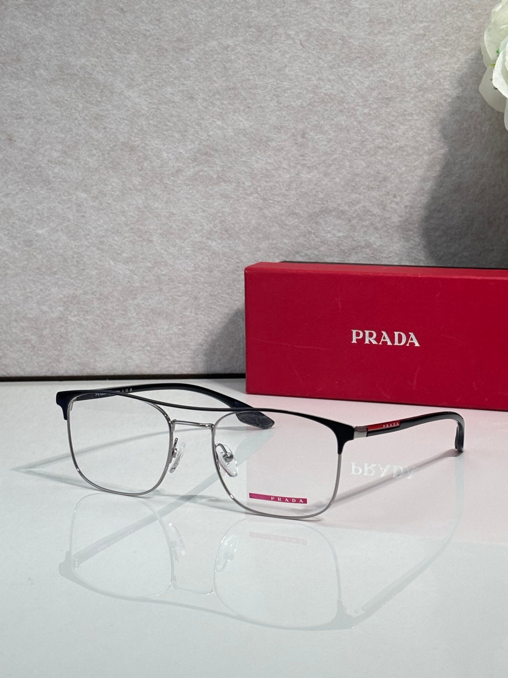Black full-rim eyeglasses with clear lenses and red logo accents, angled in front of a case.