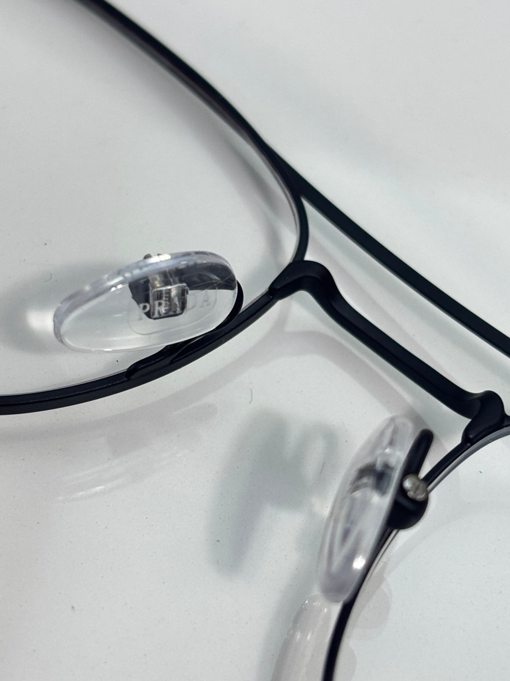 Black eyeglass frame close-up with clear lenses and visible hinge hardware.