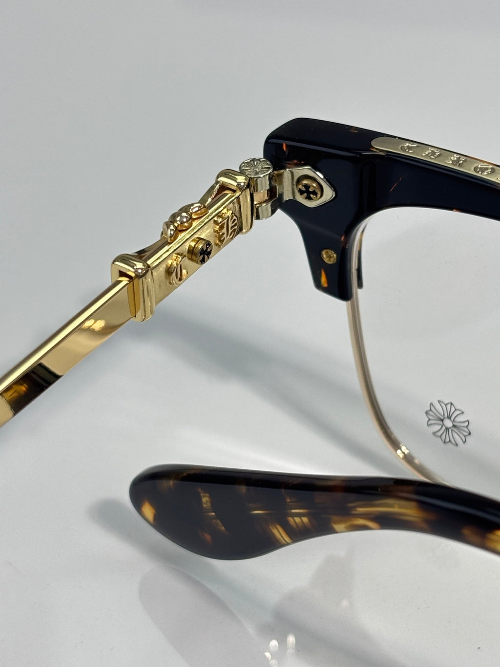Close-up of gold arm hinge and dark temple tip with flower emblem on eyeglasses