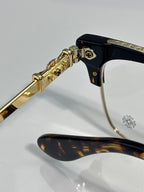 Close-up of gold arm hinge and dark temple tip with flower emblem on eyeglasses