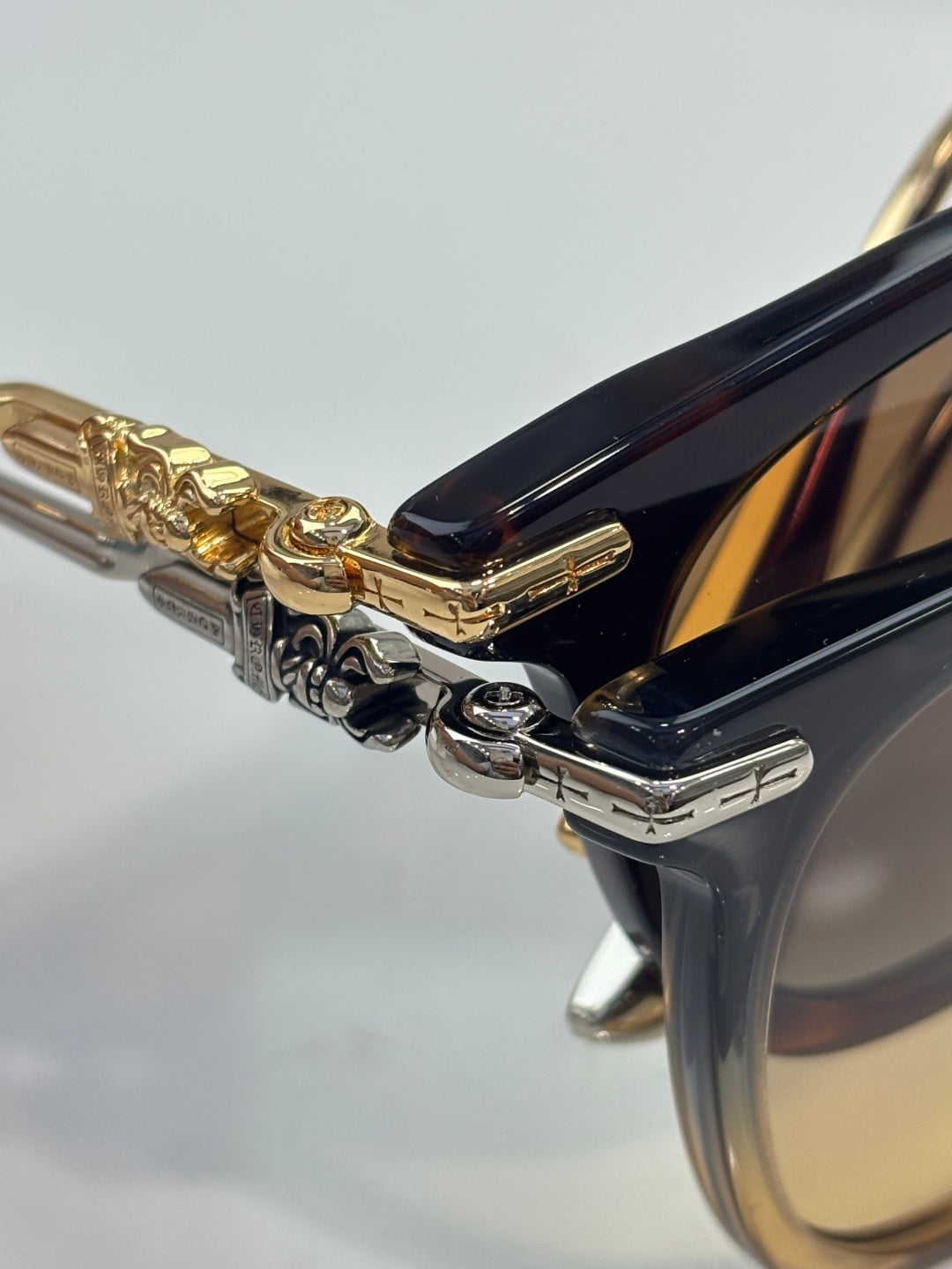 Chrome sunglasses close-up: gold-tone hinge with engraved metal and dark temples