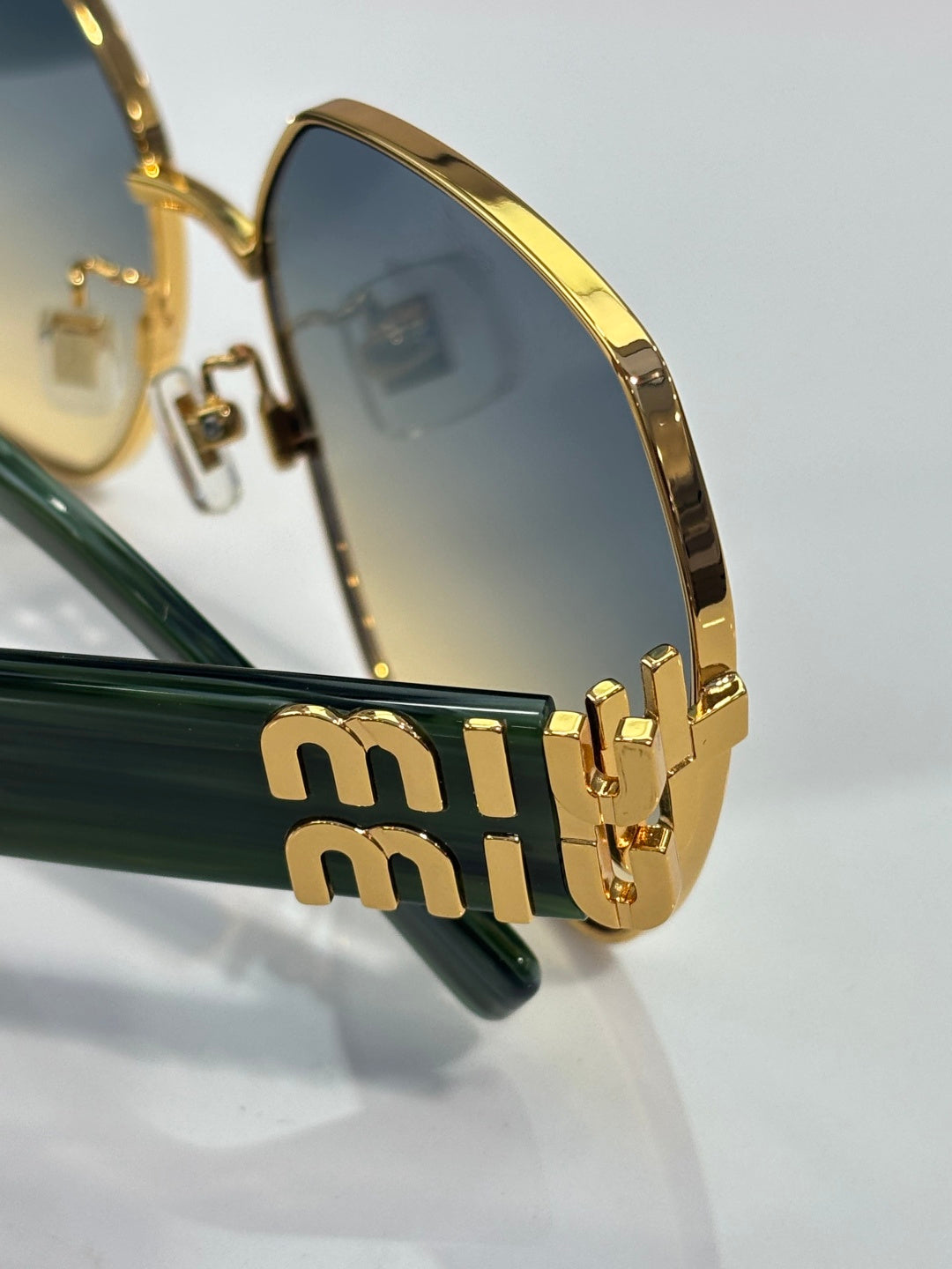 Gold-tone sunglasses temple with stacked logo detail and dark lens view