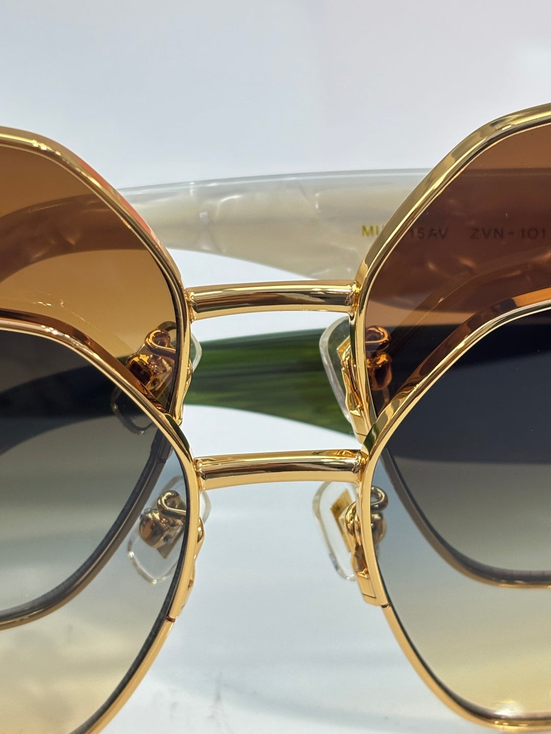 Gold-tone sunglasses with circular lenses and green bridge, front view close-up