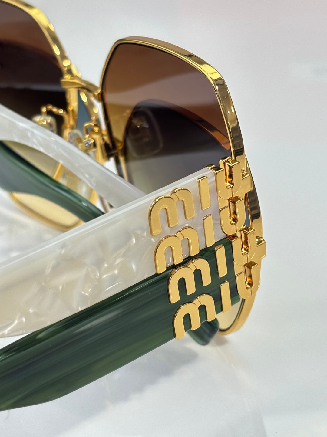 Gold-tone sunglasses showing stacked logo on temple and dark lens frame