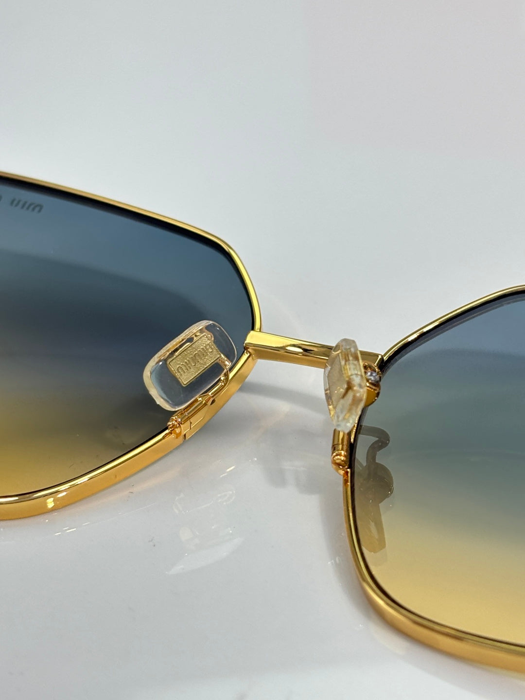 Gold-tone sunglasses showing lens edge, clear hinge piece, and thin frame detail