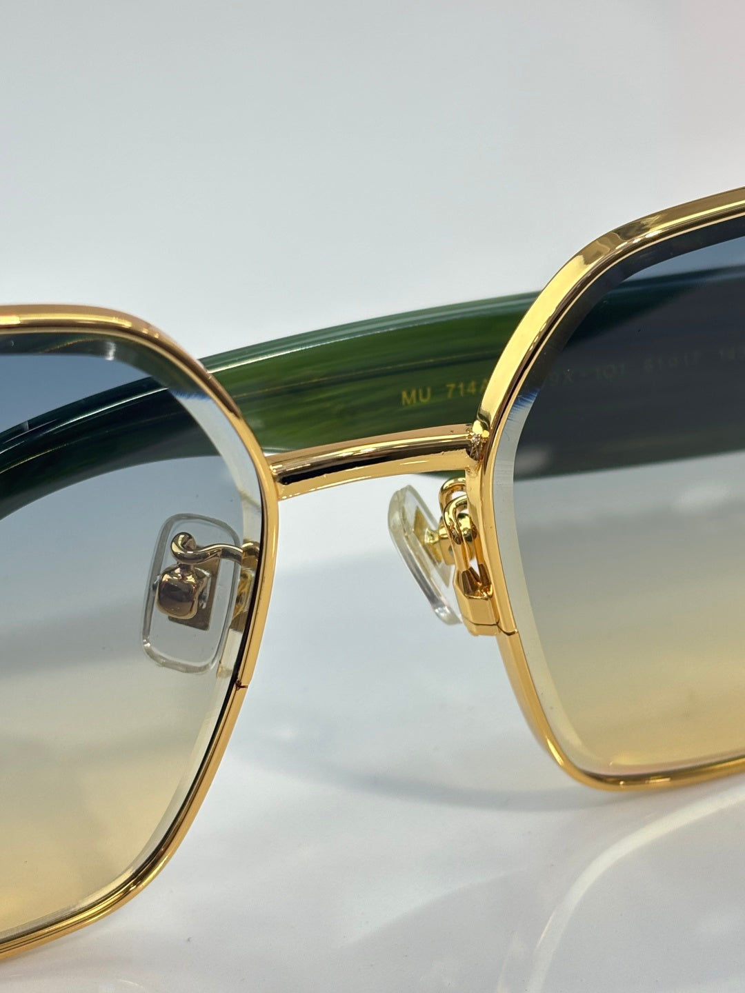 Angled view of gold sunglasses showing green striped temples and dark lens