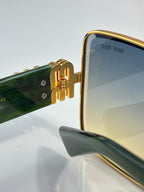 Side view of gold square sunglasses with dark lenses and green temple bar detail