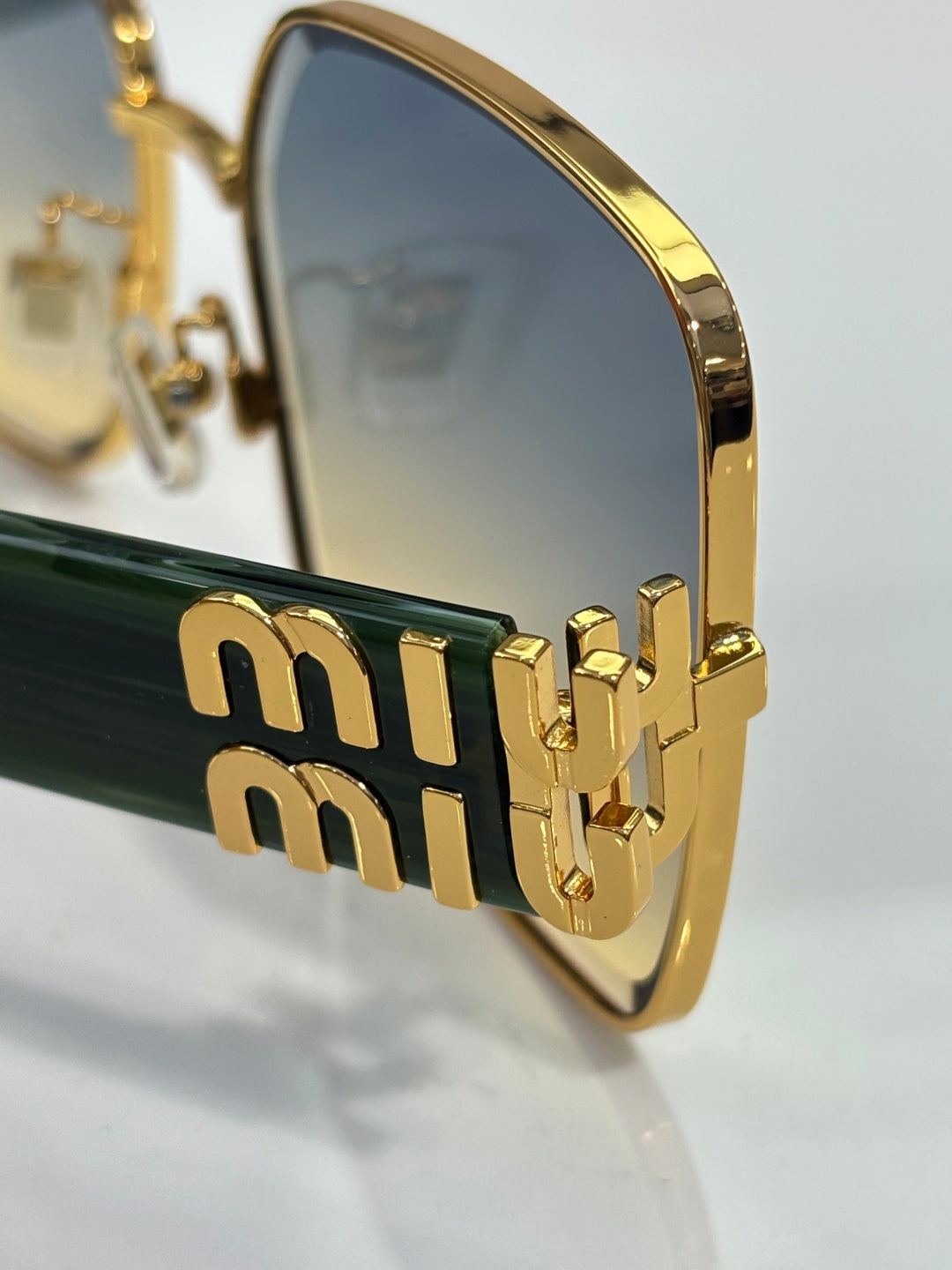 Close-up of gold temple with embossed Miu-style lettering and dark lens insert