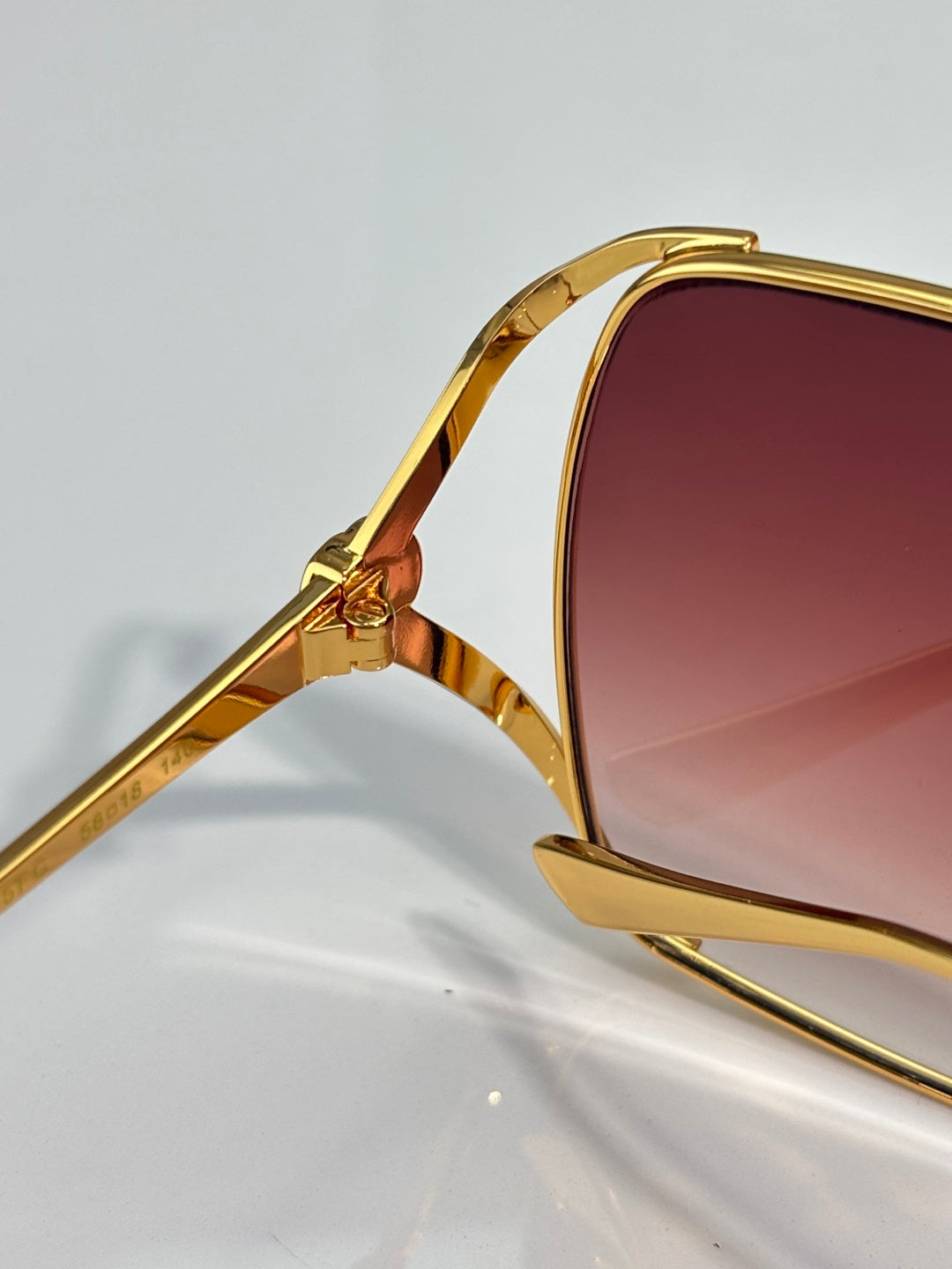 Gold-tone eyeglass arm with maroon gradient lens and hinge