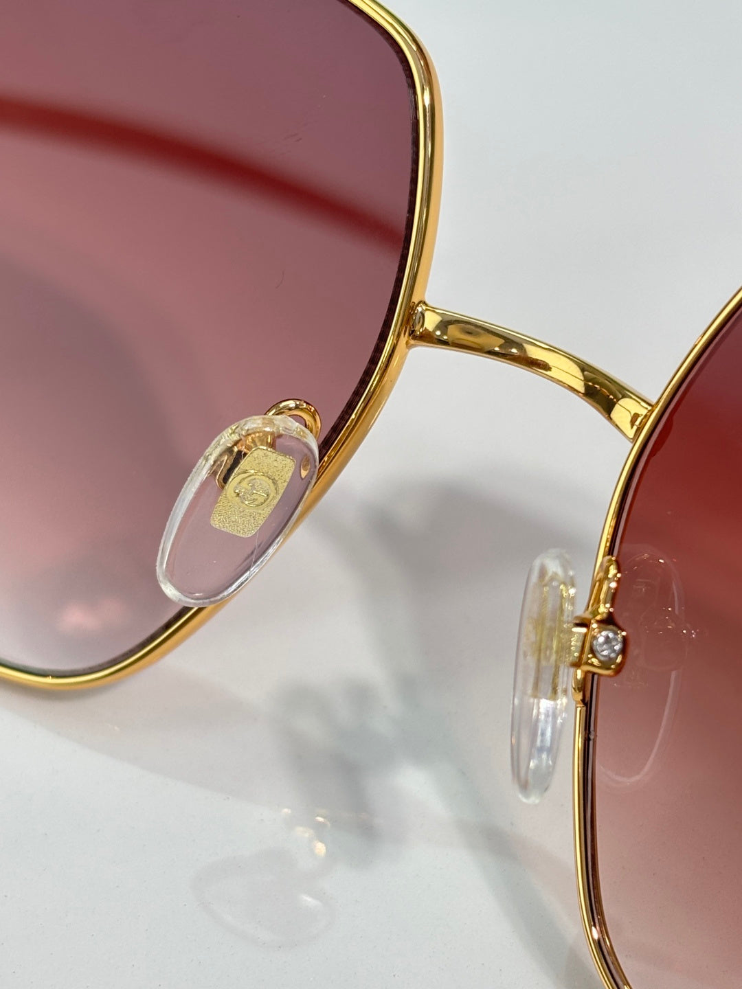 Gold-tone eyeglass frame detail with maroon gradient lens and small emblem
