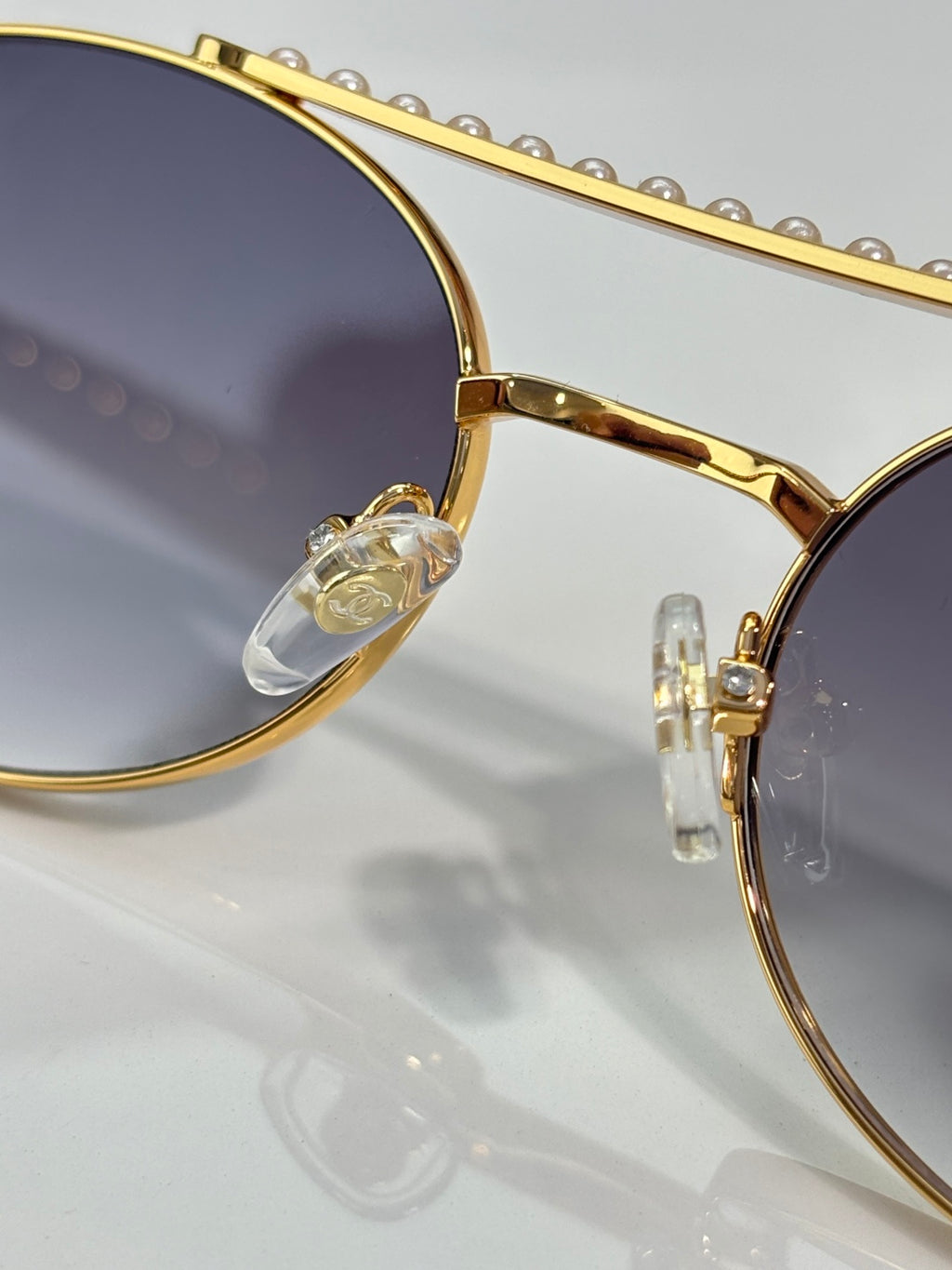 Close-up of gold round sunglasses frame with dark tinted lens and clear temple detail.