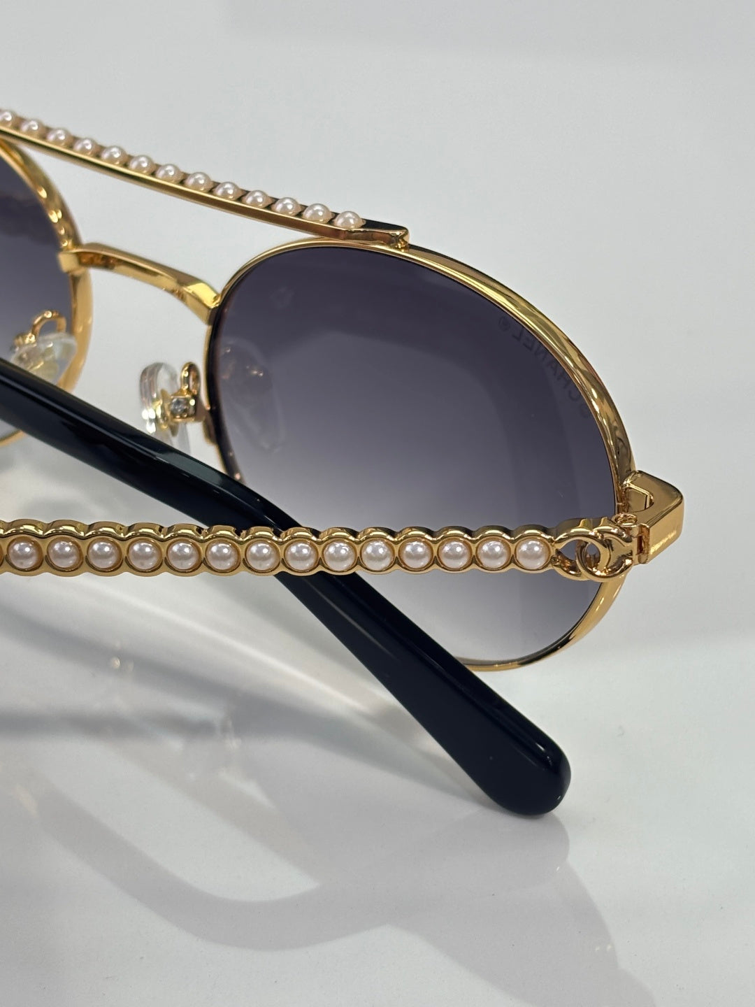 Close-up of round sunglasses with gold frame, dark tinted lens, and pearl-accented temple.
