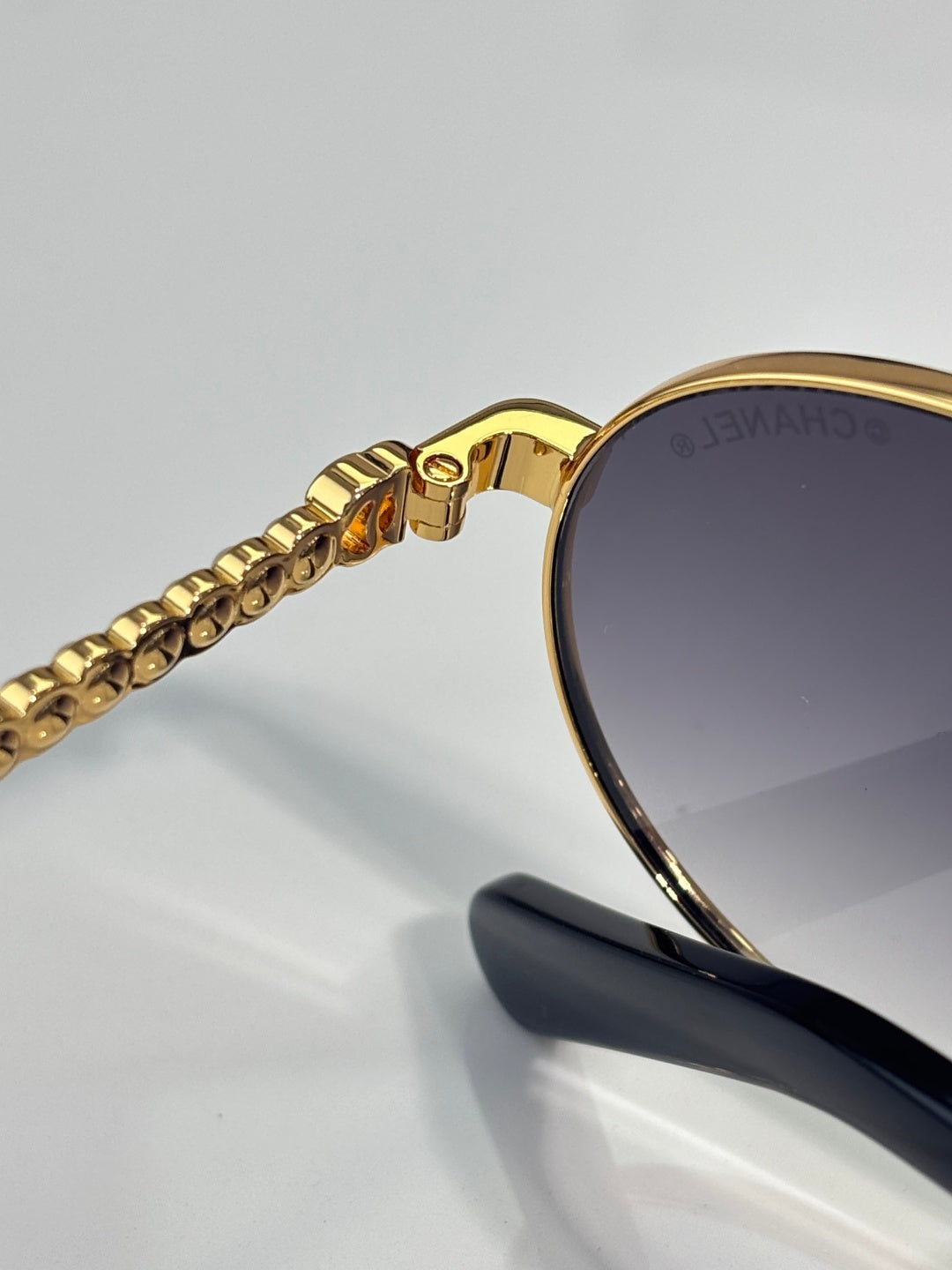 Close-up of gold sunglasses temple with beaded chain and dark tinted lens.