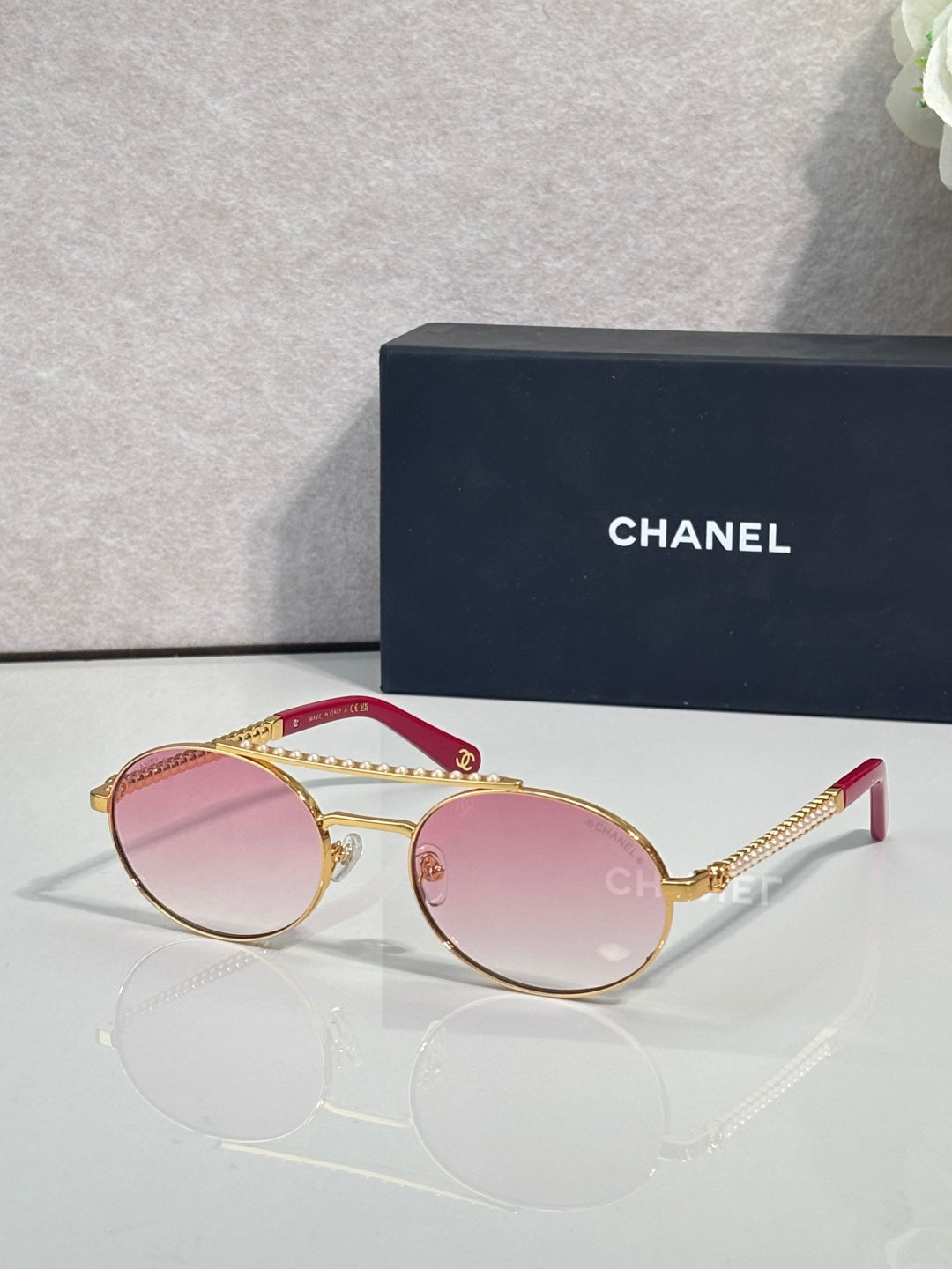 Round sunglasses with gold frame and pink tinted lenses, beaded temple detail.