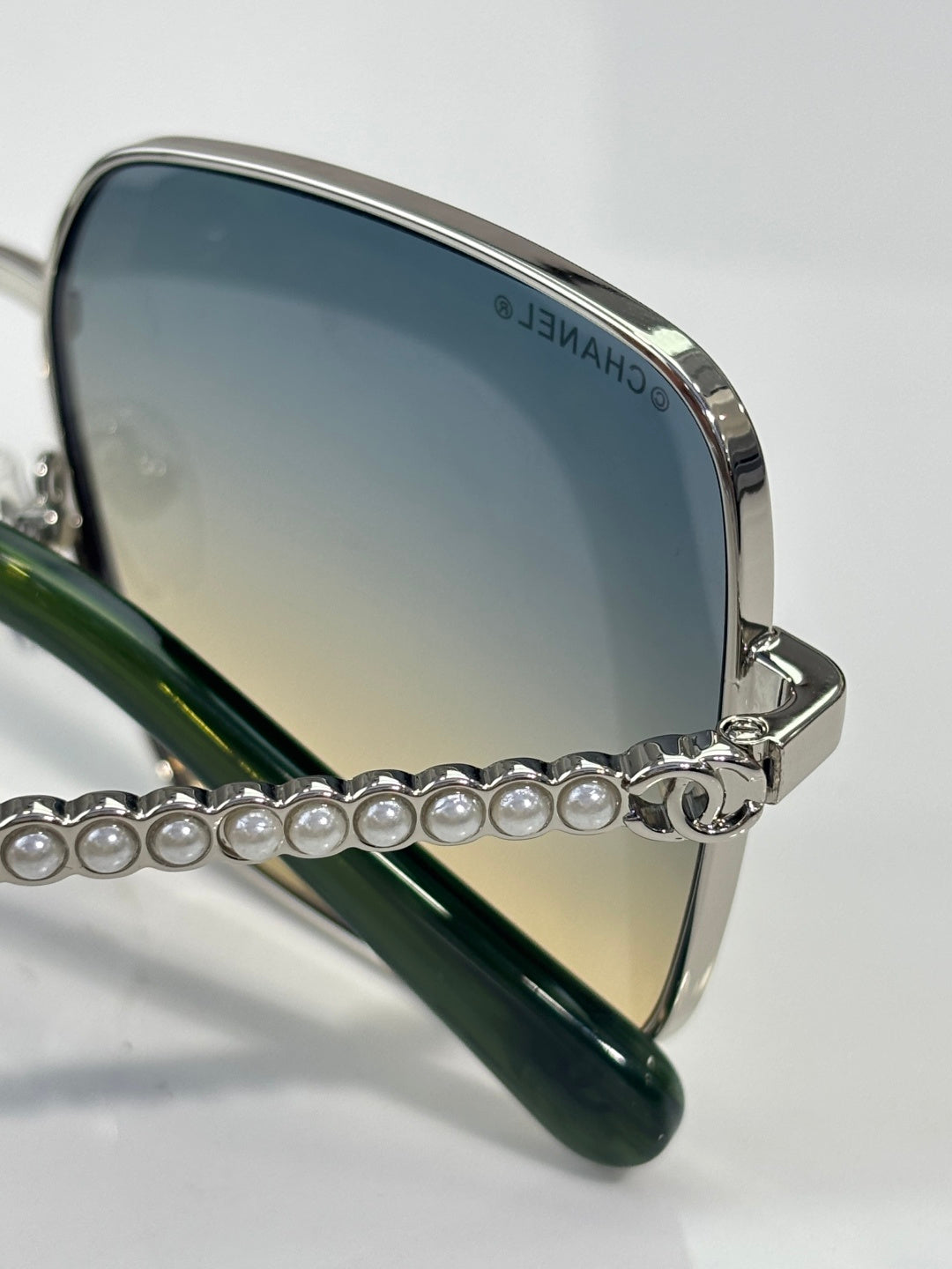 CHANEL sunglasses close-up with blue lens, green temple, pearl chain