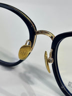 Gold-tone logo detail on navy eyeglass hinge with clear lens