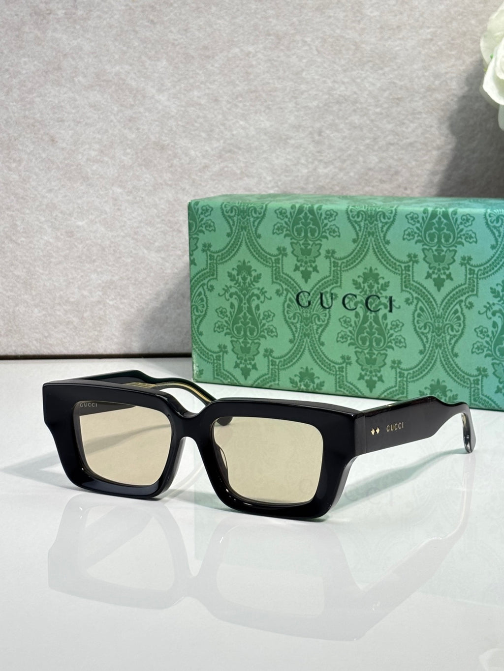 Black rectangular sunglasses with light tan lenses and Gucci logo on side arms.