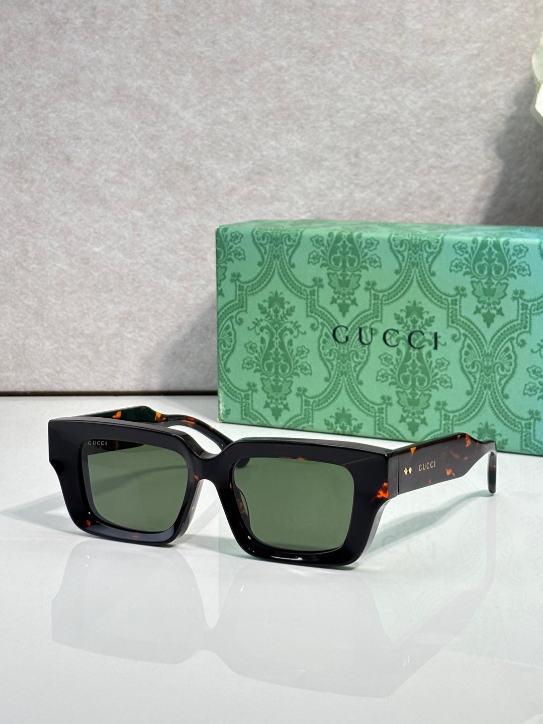 Black rectangular sunglasses with dark green lenses and Gucci logo on side arms.