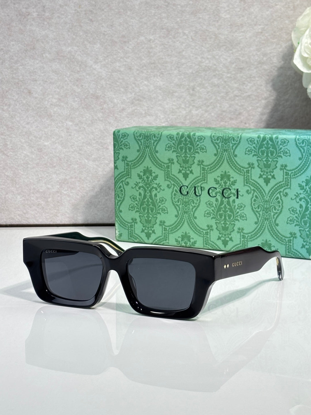 Black rectangular sunglasses with gray lenses and Gucci logo on side arms.